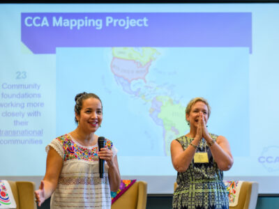 Two people stand in front of a screen displaying info about the CCA mapping project